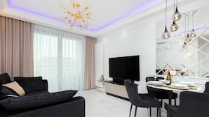 A modern living room with a black sofa, a dining table set for four, and a large flat-screen TV. - Elegant Apartment in the Center | Air Conditioning, Parking (Gdynia)