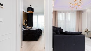 A modern hotel room with a black sofa, a bed with a black headboard, a round mirror, and a pendant light. - Elegant Apartment in the Center | Air Conditioning, Parking (Gdynia)