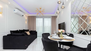 A modern living room with a black sofa, a dining table set for four, and a large window with curtains. - Elegant Apartment in the Center | Air Conditioning, Parking (Gdynia)