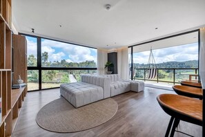 A spacious living area with a large window, a grey sectional sofa, a round rug, and a wooden dining table. - Olive 401 · PH 2 habitaciones-Jacuzzi privado en terraza y BBQ (Alto Palmas)