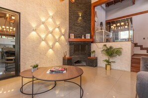 Una sala de estar moderna con chimenea, una mesa redonda llena de libros y una escalera que sube a un nivel superior.