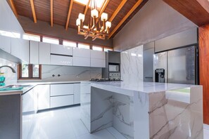 A modern kitchen with marble countertops, a built-in stove, and a stainless steel refrigerator.