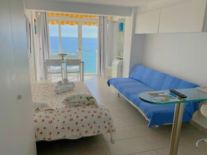 A room with a bed, a sofa, a glass table, and a view of the sea. - Estudio a Primera Línea de mar con Piscina (Platja d'Aro)