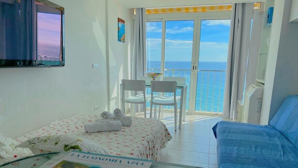 Une chambre d’hôtel avec un lit, un canapé, une table avec une brochure et un balcon donnant sur la mer.