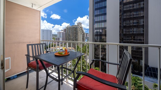 A balcony with a table and chairs, a view of tall buildings, and a clear sky.