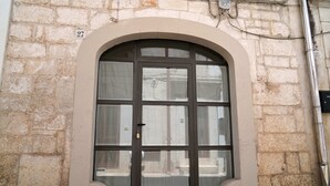 Eine Gebäudefassade mit einem großen Bogenfenster und einer Tür, mit einer Steinwand und einer Metallleitung.