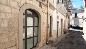 Eine enge Straße mit Steinhäusern, einem großen Rundbogenfenster und einem sichtbaren Auto auf der rechten Seite.
