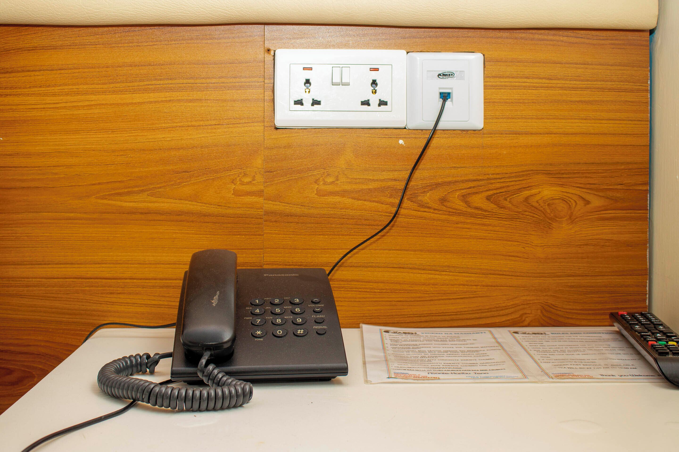 Una camera d'albergo con un telefono, un telecomando e una presa elettrica.