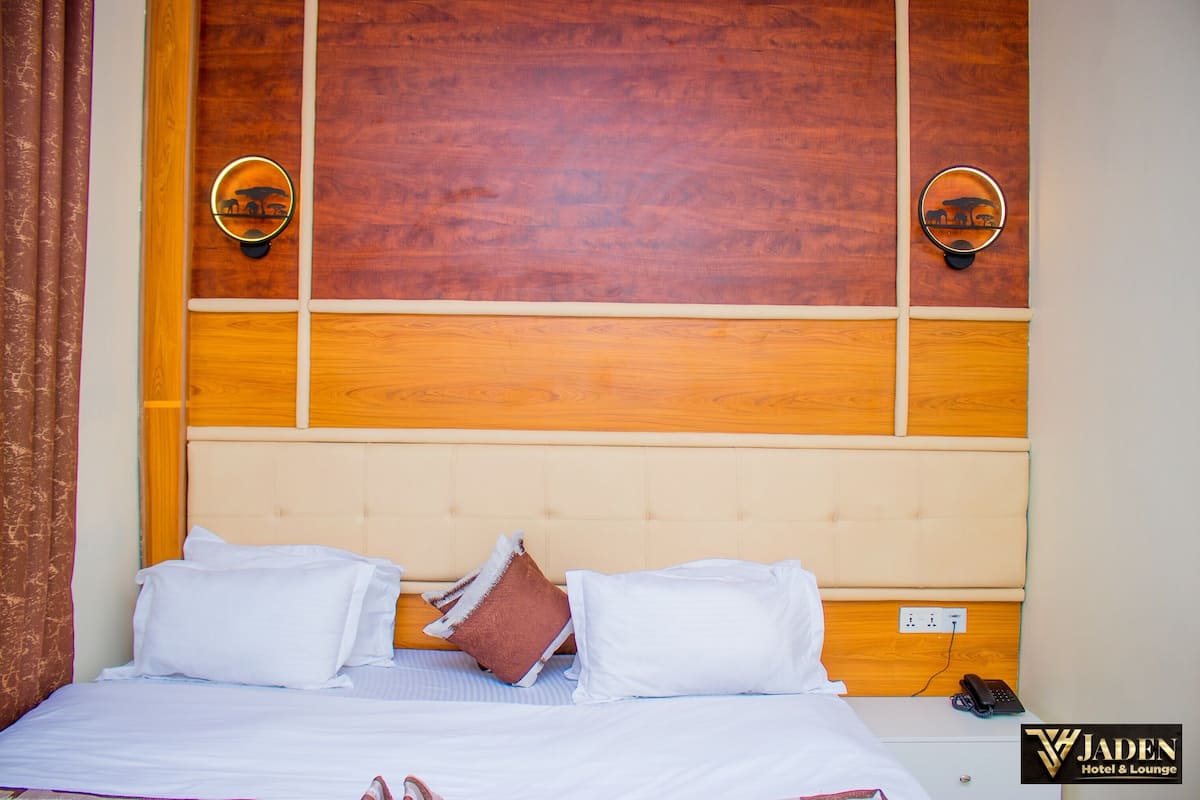 A hotel room with a wooden headboard, two wall sconces, a bed with white bedding, and a brown pillow.