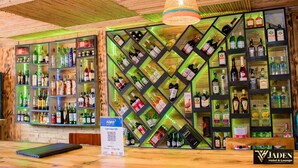 Zona de bar con estantes de madera llenos de botellas de licores, un letrero con código QR y una lámpara colgante.
