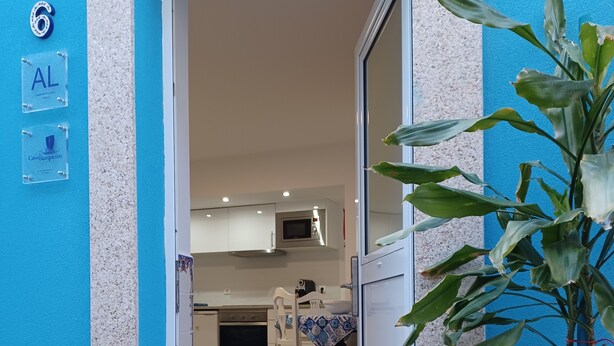 A modern apartment entrance with a blue exterior, a visible kitchen area with white cabinets, a microwave, and a dining table with chairs. - Casa Típica no Centro do Porto (PORTO)