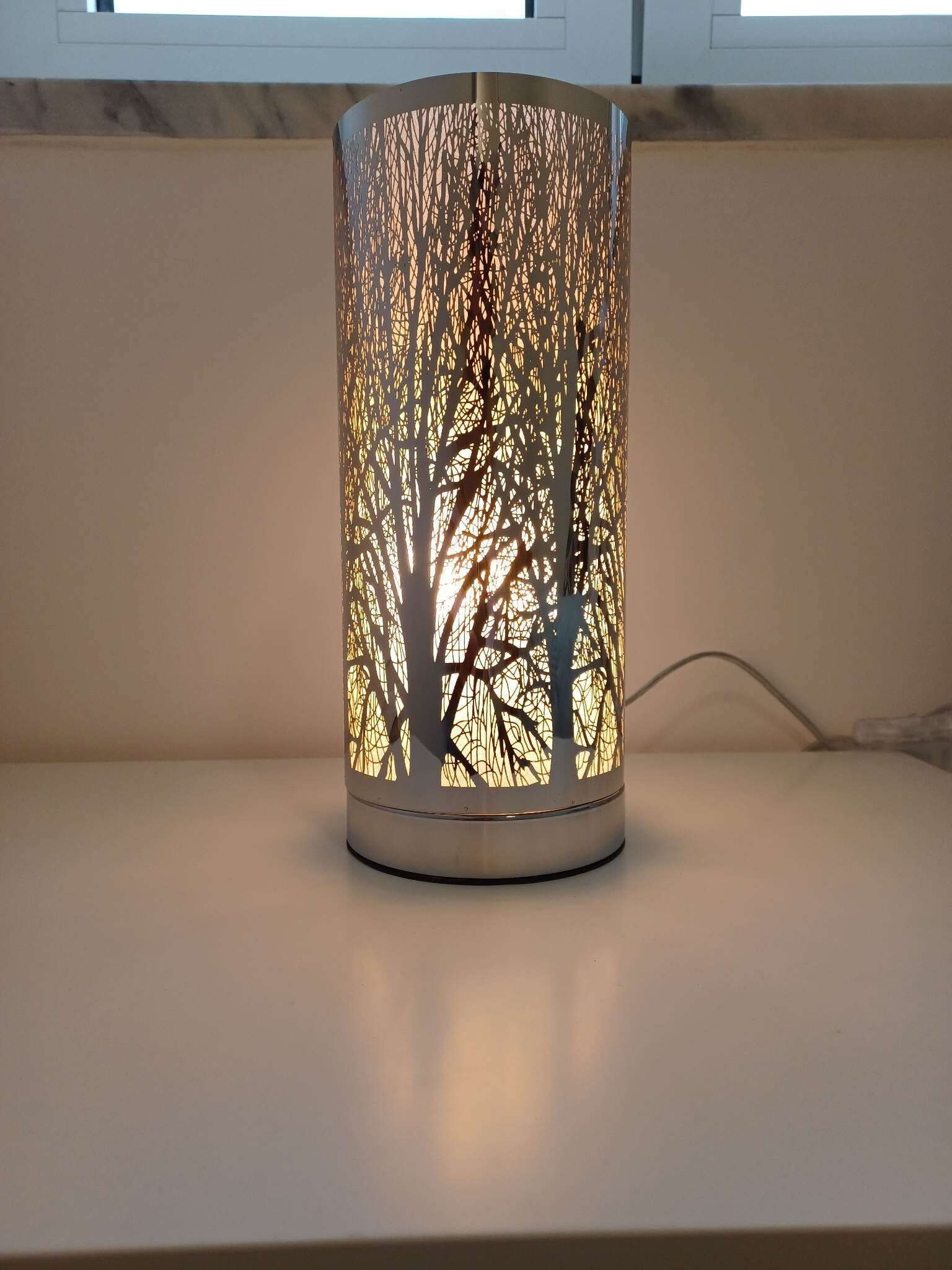 A cylindrical decorative lamp with a tree pattern, placed on a flat surface.