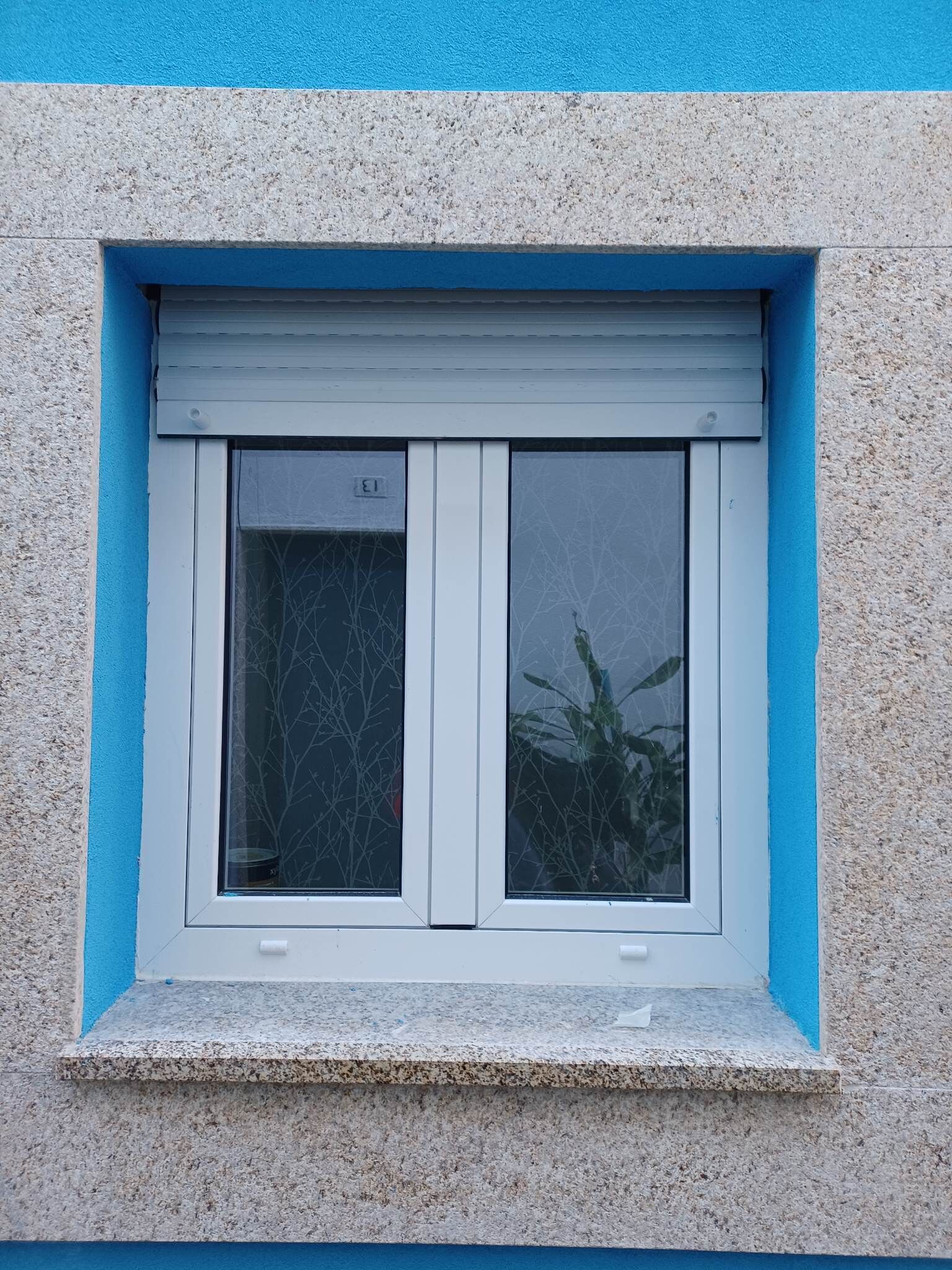 Une fenêtre dotée d’un cadre blanc et d’une bordure bleue, encadrée dans un mur à la texture particulière.