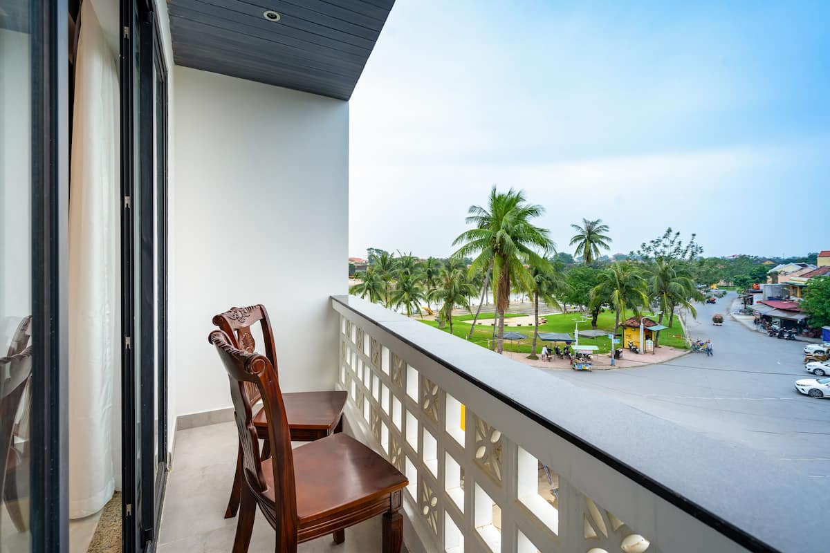 A balcony with a wooden chair and a view of a street with palm trees and buildings.