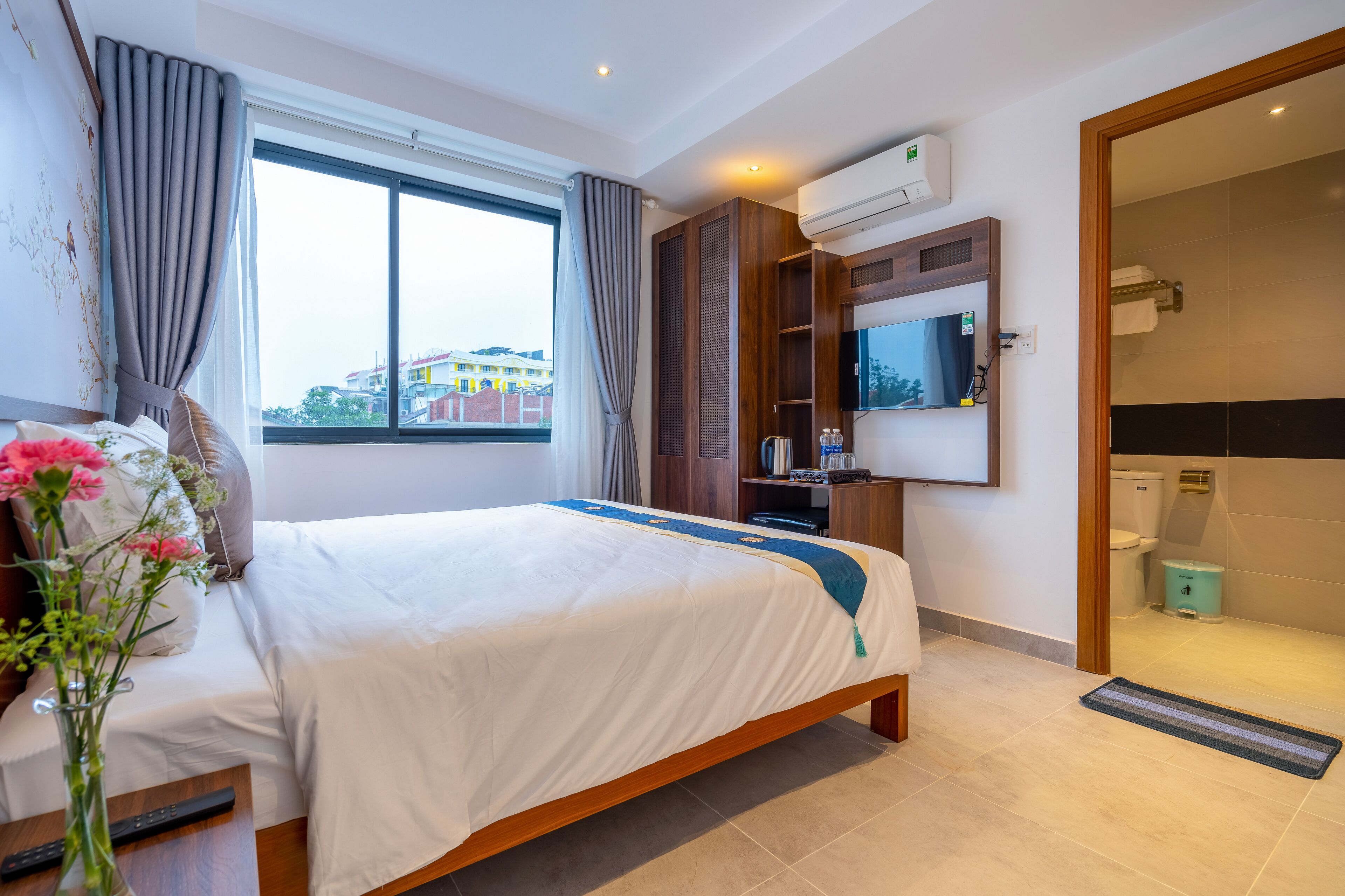A hotel room with a large bed, a TV, a wardrobe, and a bathroom visible through an open door.