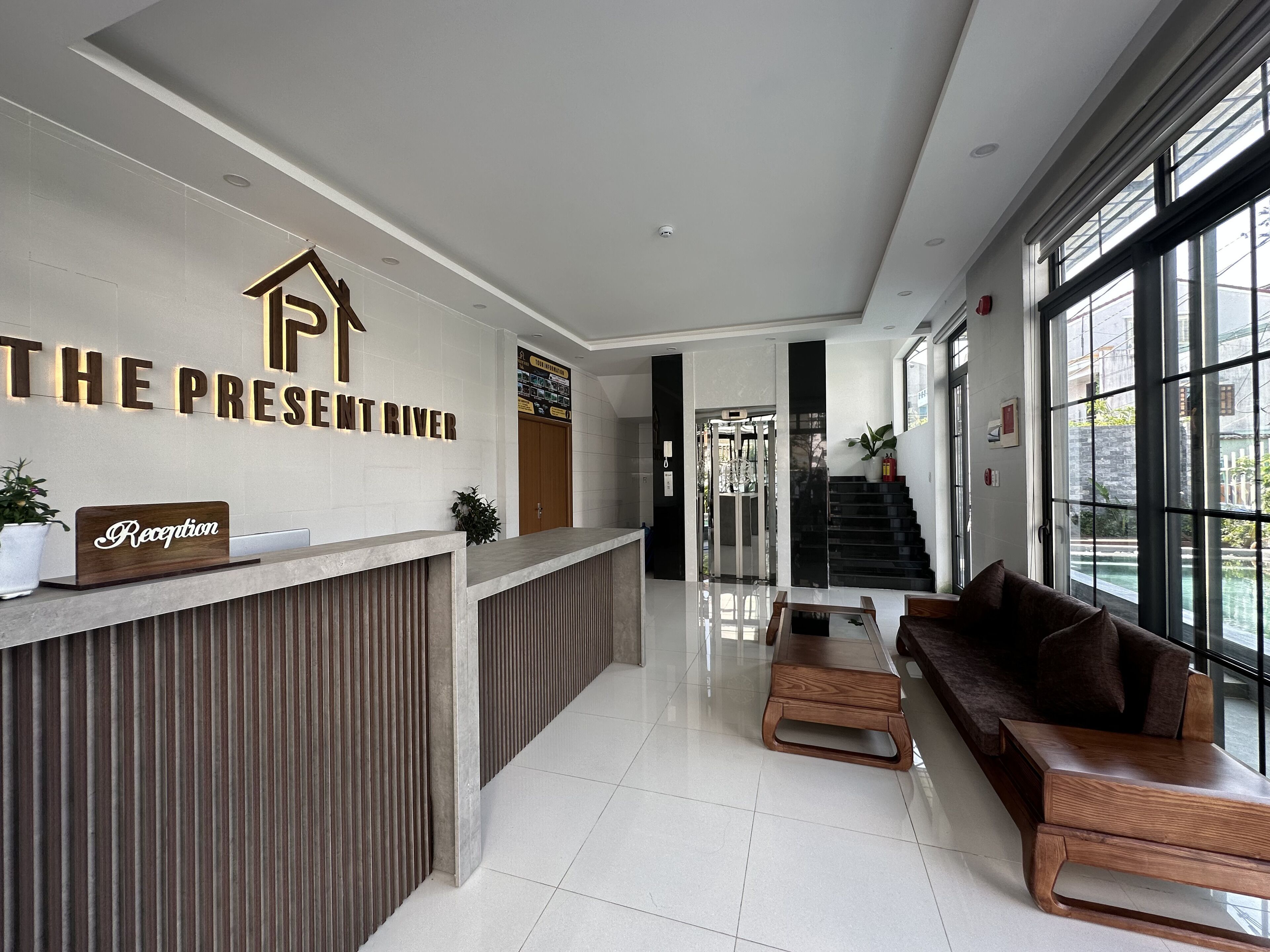A modern reception area with a reception desk, a staircase, and a seating area with a view of the outside.