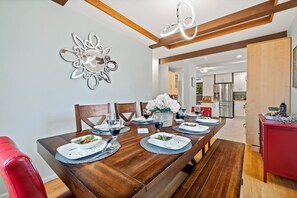 Un coin repas avec une table en bois dressée pour quatre personnes, entourée de chaises, et une cuisine en arrière-plan.