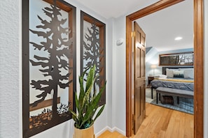 Un pasillo con una puerta de madera que da a un dormitorio con cama y una banca.