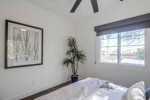 Un dormitorio con cama, un cuadro enmarcado, una planta en maceta y una ventana.