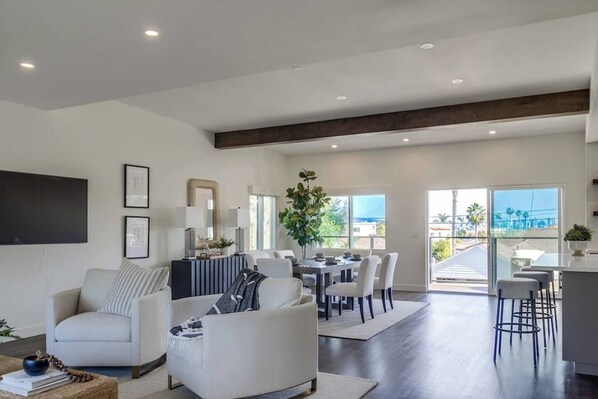 A spacious living area with a dining table and chairs, a sofa, and a kitchen area with a bar.