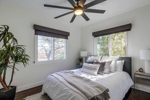 Ein Schlafzimmer mit einem Bett, zwei Nachttischen, einem Deckenventilator und einer Topfpflanze.