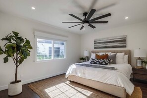 Un dormitorio con cama, ventilador de techo, ventana y planta en maceta.