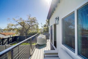Un balcón con terraza de madera, un sofá exterior blanco y un ventanal grande.