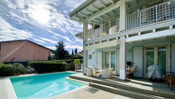 Une maison à deux étages dotée d’une piscine, de mobilier d’extérieur et d’un patio couvert.
