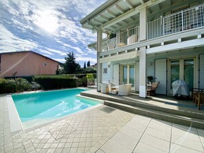 A two-story house with a swimming pool, outdoor furniture, and a covered patio area. - Villa Chiara (Polpenazze del Garda)