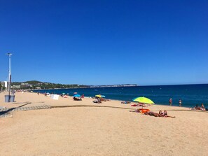 Une plage où l’on peut voir des gens se prélasser au soleil et se baigner, des parasols et un ciel bleu dégagé.