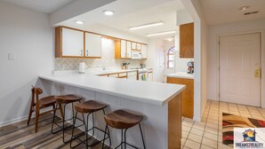 Una cocina moderna con armarios blancos, una isla grande con taburetes y un microondas a la vista.