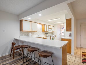 A modern kitchen with white cabinetry, a large island with bar stools, and a visible microwave.