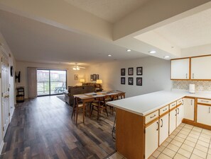 A spacious living area with a dining table, a sofa, and a kitchen with wooden cabinets and a tiled backsplash.