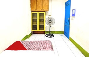 Une pièce avec un meuble en bois, une porte bleue, un ventilateur et un tapis à motifs.