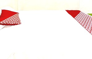 A room with a white bedspread and red pillows with a repeating pattern.