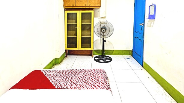 Una habitación con cama, ventilador, puerta azul y un armario de madera.