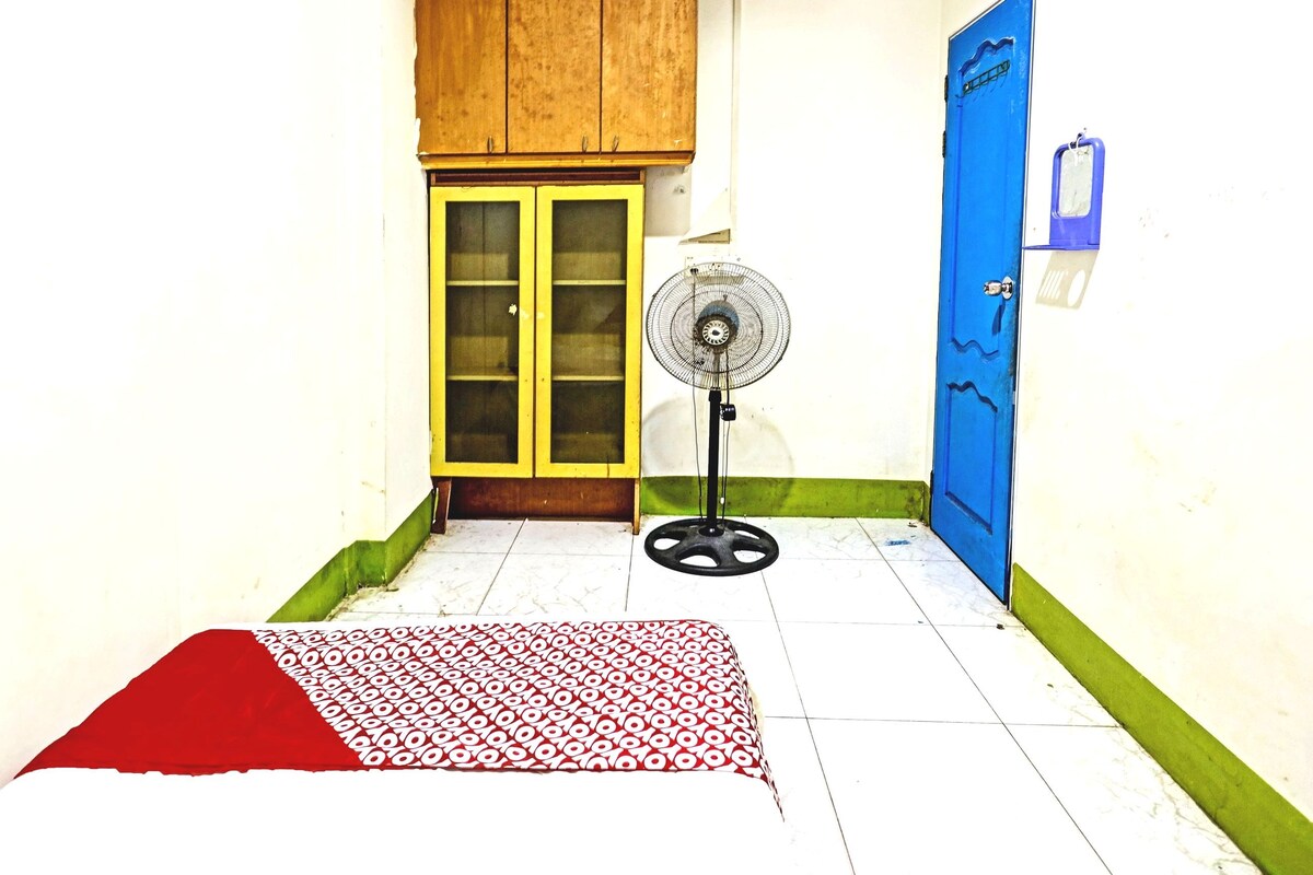 A room with a bed, a fan, a blue door, and a wooden cabinet.