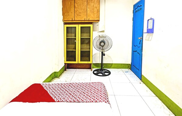 Une pièce avec un lit, un ventilateur, une porte bleue et une armoire en bois.