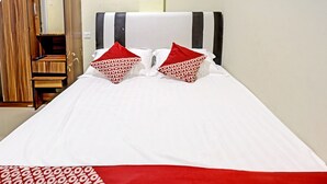 Una cama con ropa de cama blanca y roja, un armario de madera y un cabecero a rayas.