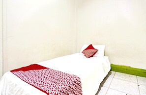 Une petite pièce simple, avec un lit, une couverture à motifs rouges et blancs, et un oreiller aux motifs similaires.