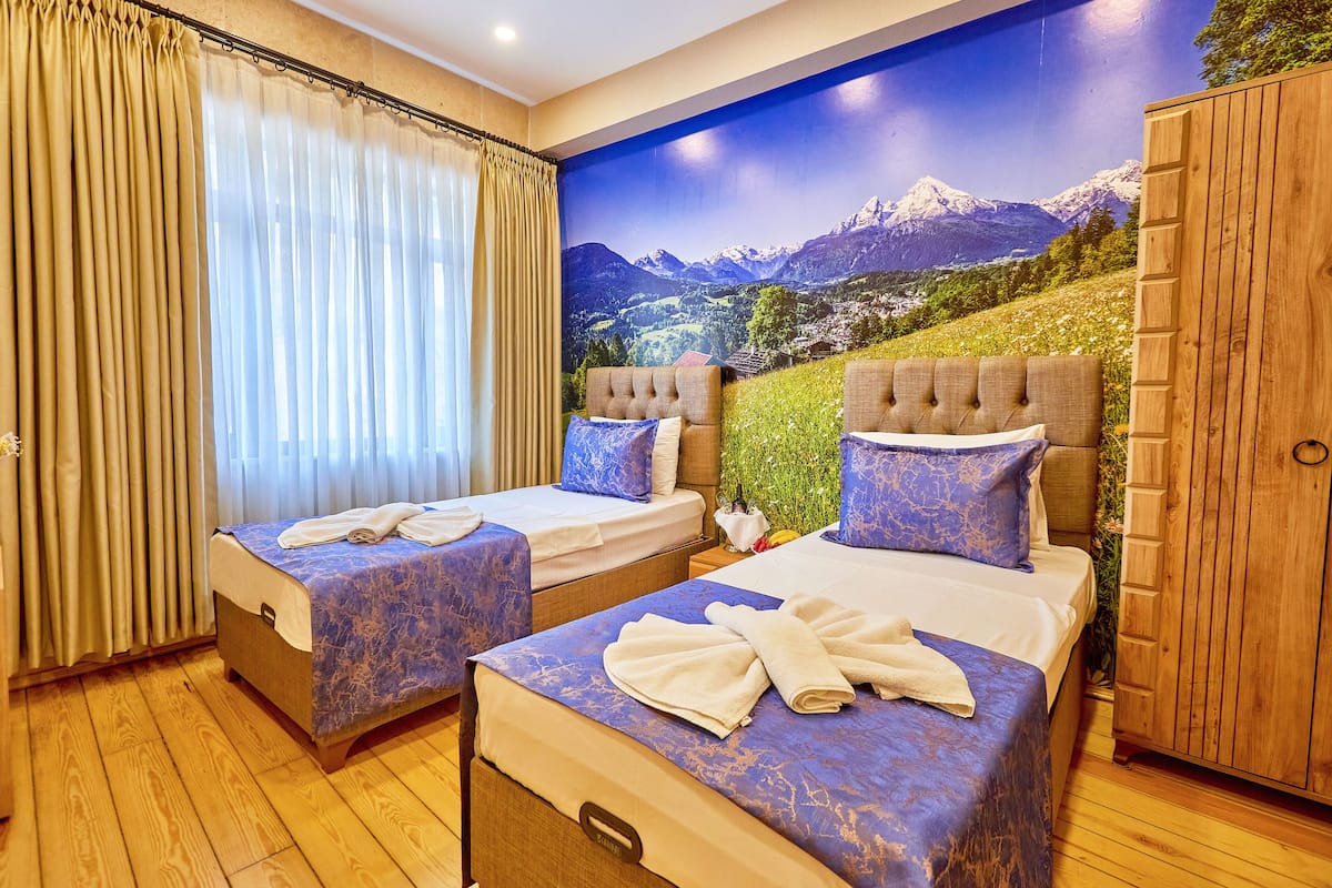 A hotel room with two beds, a wooden wardrobe, and a scenic mountain view mural.