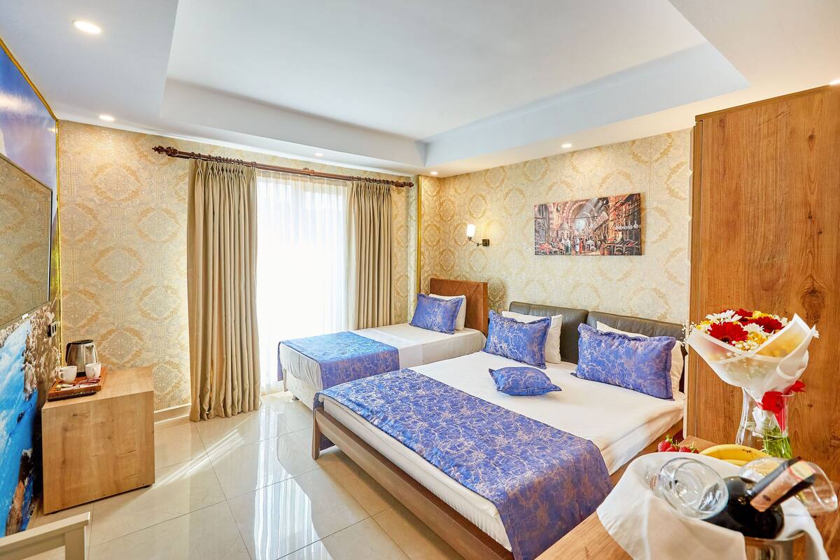 A hotel room with two beds, a wooden side table, a large mirror, and a painting on the wall.
