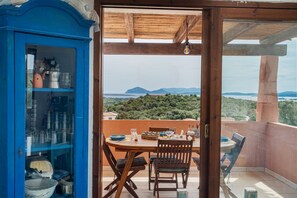 Ein Balkon mit einem Holztisch, gedecktem Esstisch, einem blauen Küchenschrank mit Geschirr und einer herrlichen Aussicht auf Berge und Grün.
