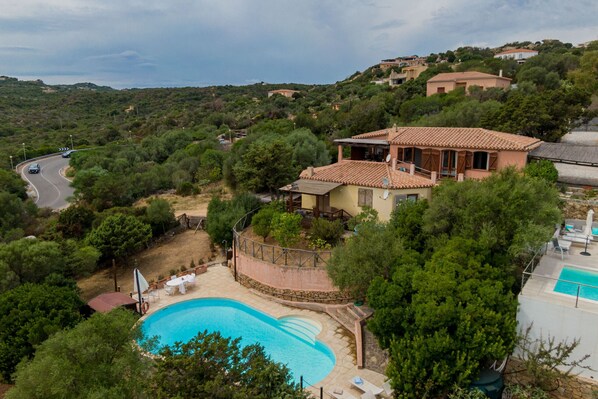 Une maison avec une piscine, entourée d’arbres et de collines.