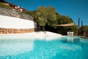 Una piscina azul cristalina con un muro de piedra y una terraza de madera.