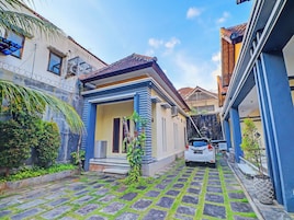 Rua estreita com uma pequena casa, teto telhado e um carro estacionado na frente.