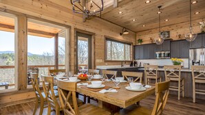 Un intérieur en bois comprenant un coin repas, une cuisine et de grandes fenêtres donnant sur l’extérieur.