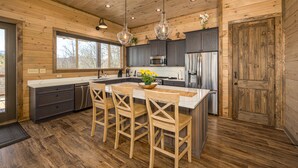 Une cuisine rustique, située dans une cabane en bois, avec un îlot central, des tabourets de bar et des luminaires suspendus.