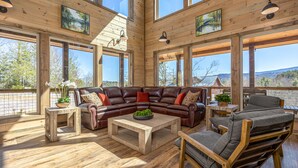 Un salon spacieux, doté d’un grand canapé d’angle en cuir, d’une table basse en bois et offrant une vue sur l’extérieur grâce à de grandes fenêtres.