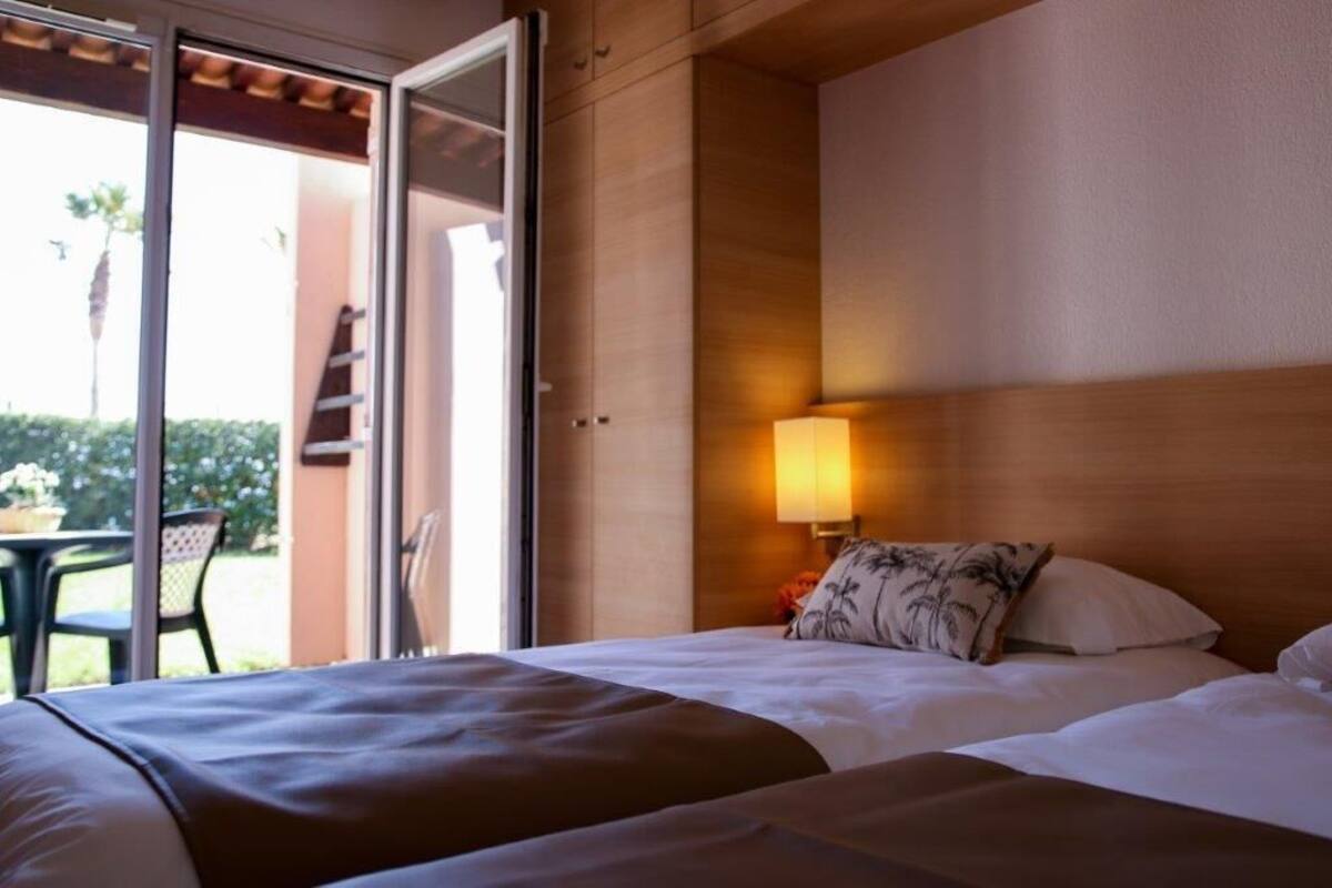 Quarto de hotel com cama, mesa de cabeceira com abajur e porta de vidro deslizante para área externa.